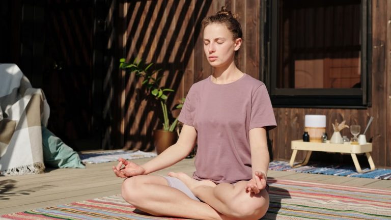 Woman practicing meditation in lotus pose on a sunny outdoor deck.
