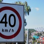 Close-up of a 40 km/h speed limit sign near a chain-link fence and urban landscape.